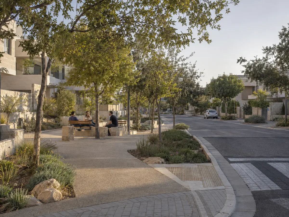 רחוב קהילתי בהרחבה יישובית עם מדרכות מוצלות וצמחייה מותאמת אקלים